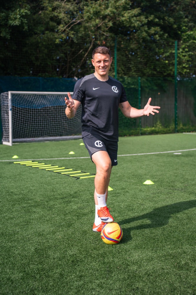 Coach Kier on the pitch with a ball, in front of goal
